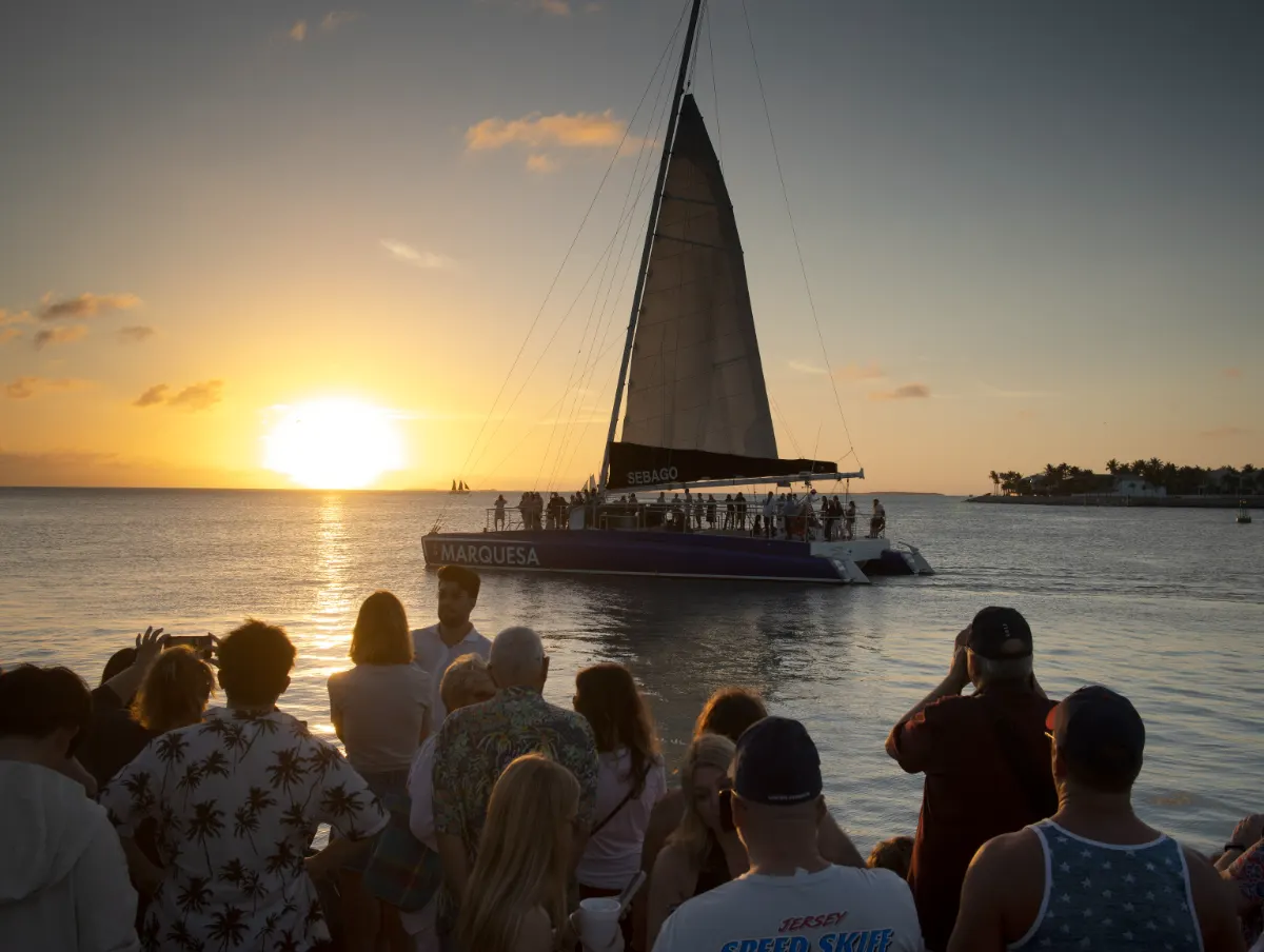 Catamaran packed with passengers sailing past the sunset crowd at Mallory Square