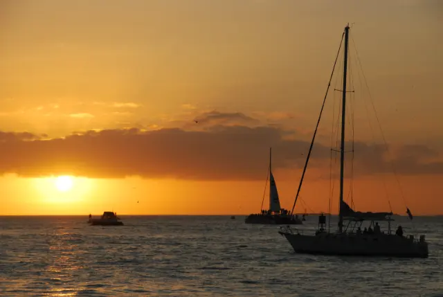 Small sailboat with a few people aboard at sunset off Mallory Square, Key West