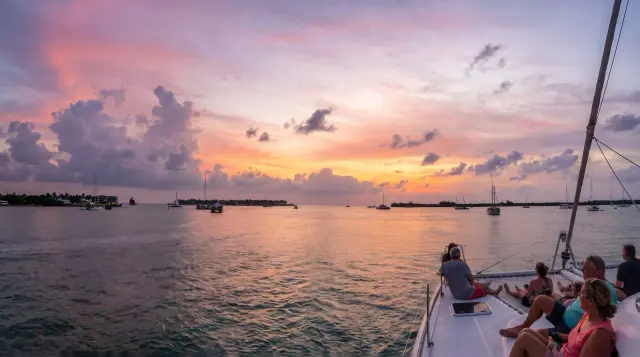 Guests relaxing on the bow of a sailing catamaran under a pink and purple Key West sunset sky